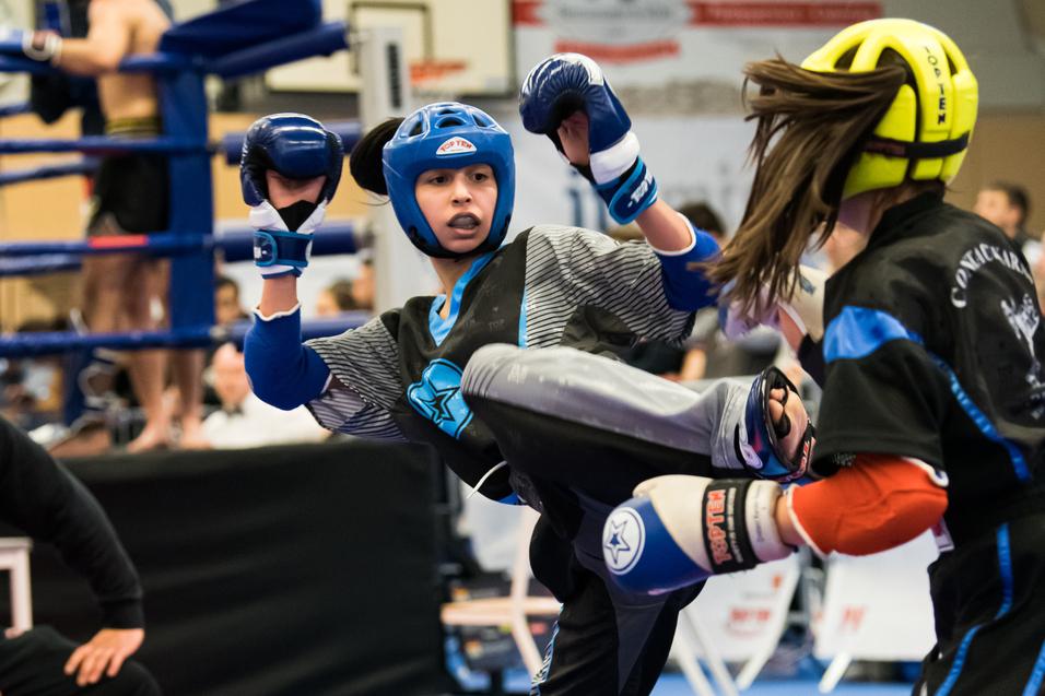 Zwei Kämpferinnen im Kickboxen, eine tritt mit dem Bein aus einem Kampfstand auf einen Mattenboden.